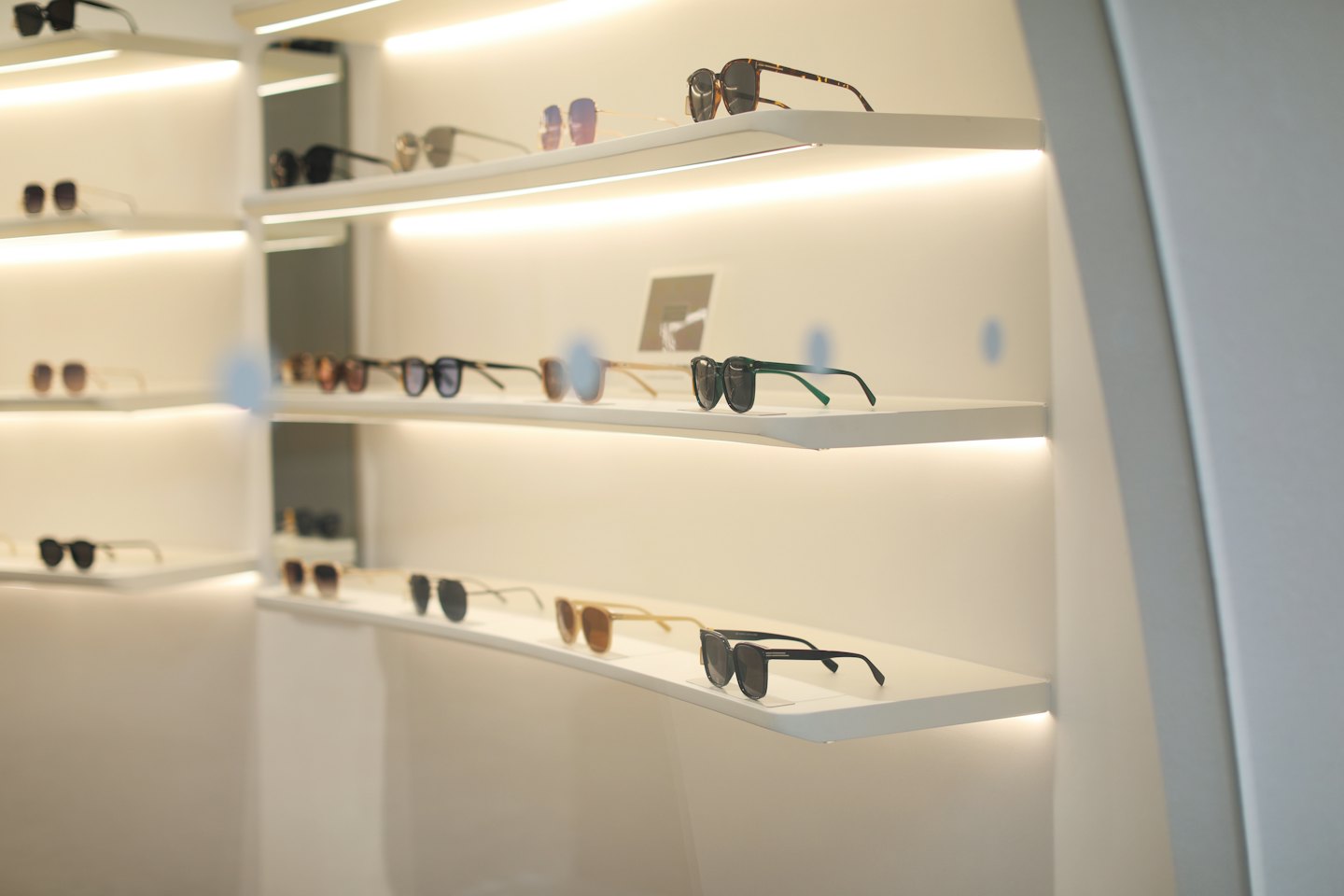 Occhiali da sole alla moda esposti ordinatamente su scaffali bianchi e puliti per la vendita al dettaglio.